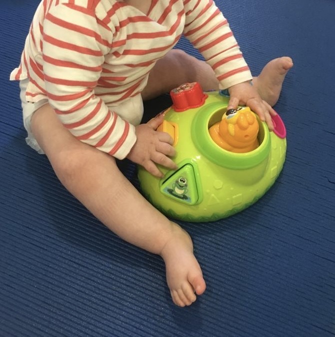 Bebé sentado jugando con un juguete musical interactivo en un suelo azul.