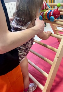 Niña pequeña subiendo una escalera de madera con la ayuda de un adulto.