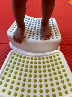 Pies de un niño parado sobre un escalón de plástico con superficie antideslizante.